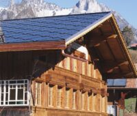 Ein traditionelles Haus in den Alpen mit einen Dach, das Solarziegel von Sun Style bedecken.