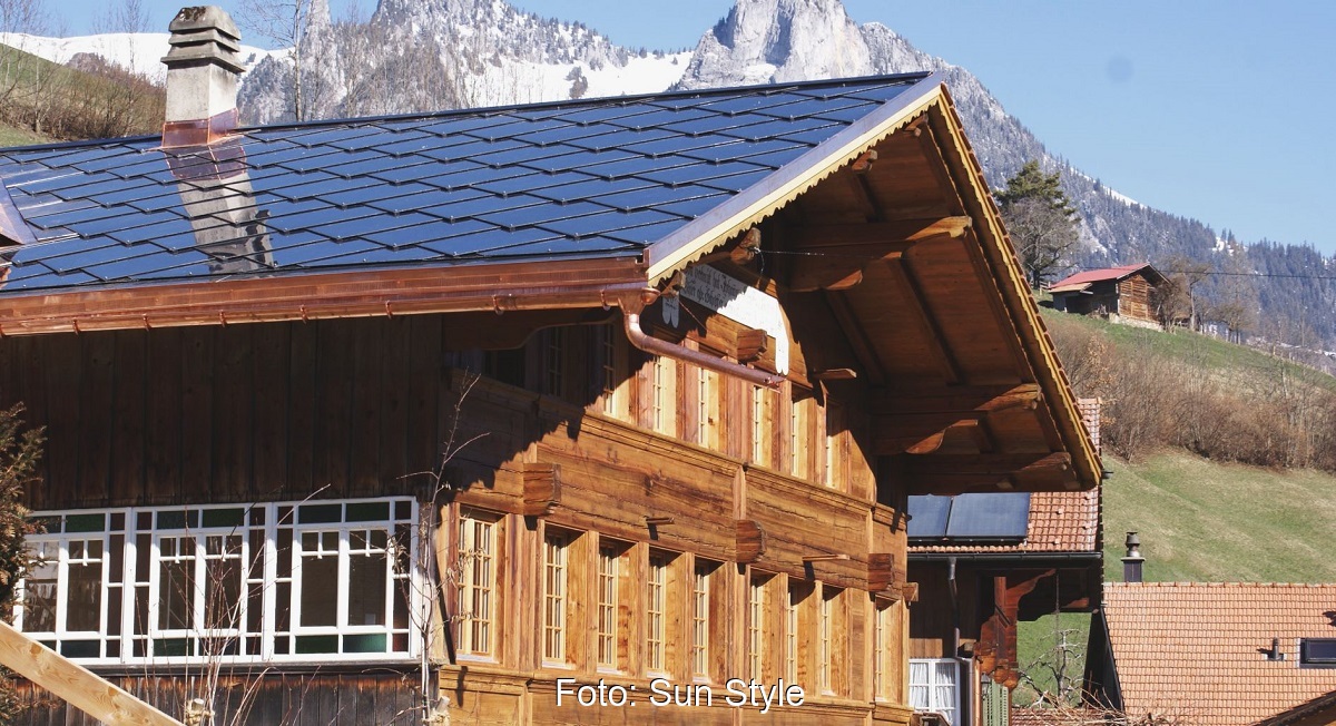 Ein traditionelles Haus in den Alpen mit einen Dach, das Solarziegel von Sun Style bedecken.