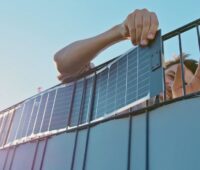 Ein Mensch fädelt die flexiblen Solarstreifen in einen Stabmattenzaun.