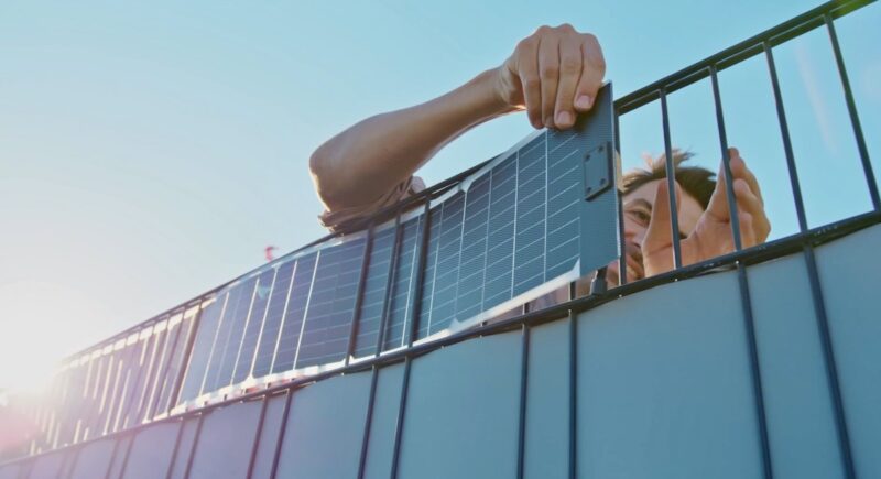 Ein Mensch fädelt die flexiblen Solarstreifen in einen Stabmattenzaun.