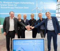 Mehrere Manager und eine Politikerin reichen sich die Hand vor einer Präsentation über den ersten direkten Windstromliefervertrag für die industrie in Deutschland.
