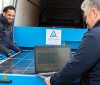 Im Bild zwei Männer, die ein Photovoltaik-Modul im Mobile Solar Lab des TÜV Rheinland testen.