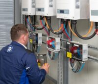 Im Bild ein Mann, der Wechselrichter einer Photovoltaik-Anlage prüft, TÜV Süd kooperiert mit der Zurich-Versicherung.