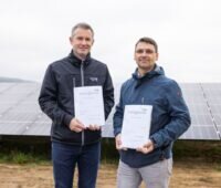 Zwei Männer mit je einem Vertragsexemplar in den Händen vor einer Freiflächensolaranlage.