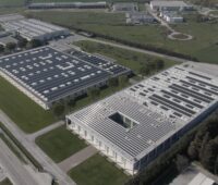 Luftbild eines Unternehmenskomplexes mit drei Gebäuden, von denen eines eine PV-Dachanlage hat.