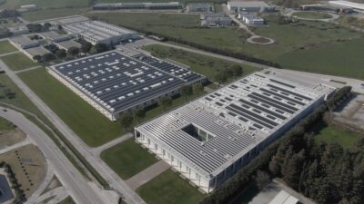 Luftbild eines Unternehmenskomplexes mit drei Gebäuden, von denen eines eine PV-Dachanlage hat.