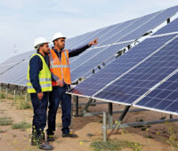 Zwei Arbeiter mit Signalwesten vor Photovoltaikmodulen Eines PV-Parks in Tunesien