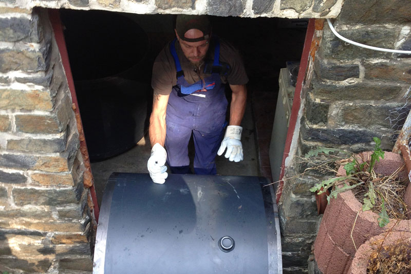 Zylinderförmiges Speichersegment wird von einem Handwerker durch eine schmale Kellertür bugsiert