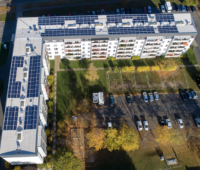 Luftfoto von L-förmigem Mehrfamilienhaus, mit Photovoltaik-Anlage auf dem Dach - Vonovia erzeugt Solarstrom in Dresden.