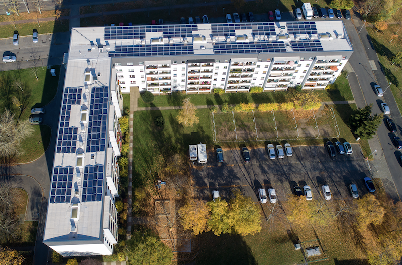 Luftfoto von L-förmigem Mehrfamilienhaus, mit Photovoltaik-Anlage auf dem Dach - Vonovia erzeugt Solarstrom in Dresden.