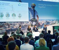 Konferenz mit vier Personen auf dem Podium und Fotos der Windenergie.