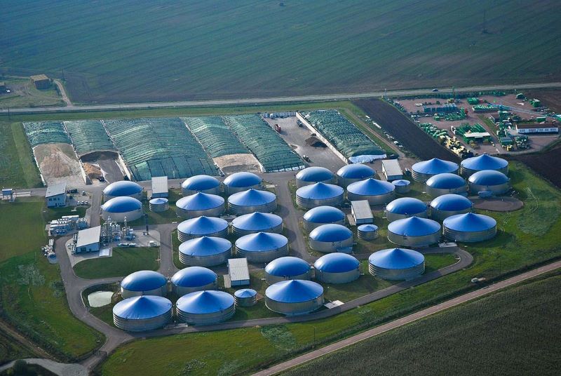 Luftbild mit zwei Dutzend blauen Biogasfermentern in grüner Wiesenlandschaft.