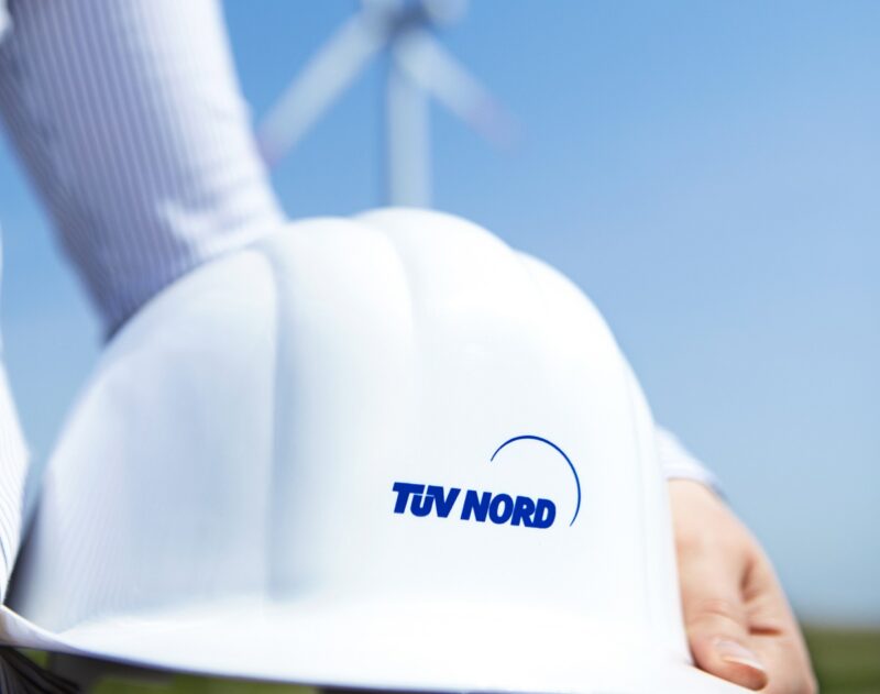 Zu sehen ist ein Schutzhelm mit TÜV Nord Logo als Symbol für den komplexen Bau von Windenergie-Anlagen in Störfallbetrieben.