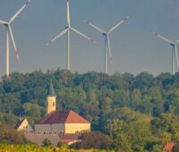Windpark in Bayern, Zöschingen, drei Windenergie-Anlagen hinter einer Kirche. Symbol für Erneuerbare Energien.