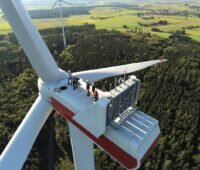 Luftaufnahme auf die Gondel einer Windenergie-Anlage, dort stehen Menschen. Symbolbild für Rolle der Kommunen bei Energiewende.