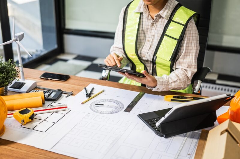 Mensch am Schreibtisch mit Windenergie-Modell und CAD-Unterlagen - Symbol für Planung und Genehmigung von Windenergie-Anlagen