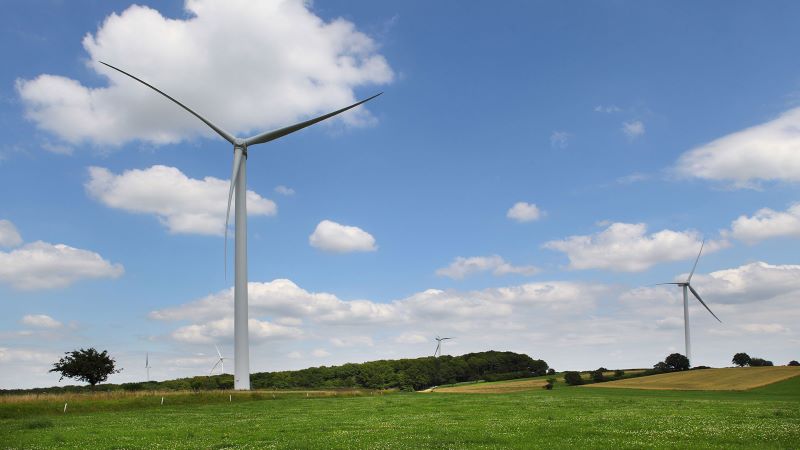 Windkraftanlagen in Wiesenlandschaft mit blauem Himmel und Schäfchenwolken.