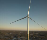 Foto von Windturbine mit Hybridturm von Nordex - man erkennt den unteren Teil des Turms aus Beton in grau, den oberen aus Stahl in weiß.