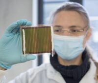 Zu sehen ist eine Forscherin, die eine Solarzelle mit Tandem-Solartechnologie für die Photovoltaik der Zukunft in Händen hält.