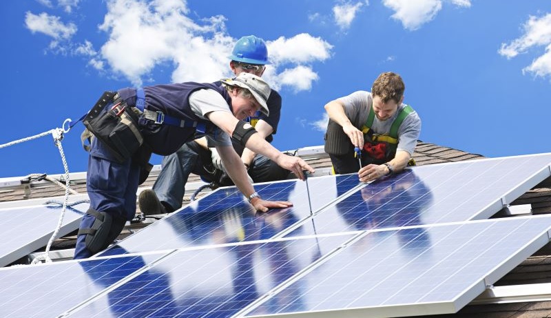 Im Bild drei Männer, die eine Photovoltaik-Anlage festschrauben, eine Branchenvereinbarung soll den Arbeitsschutz bei der Montage gewährleisten.