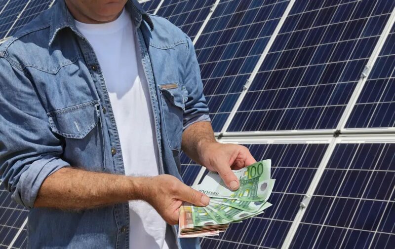 Im Bild ein Mann mit Geldscheinen vor Solaranlage als Symbol für die Ratenzahlung für Photovoltaik-Anlage von Zolar.