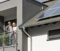Ein Ehepaar betrachtet zufrieden von einer Loggia aus die Photovoltaikanlagen auf dem Schrägdach.