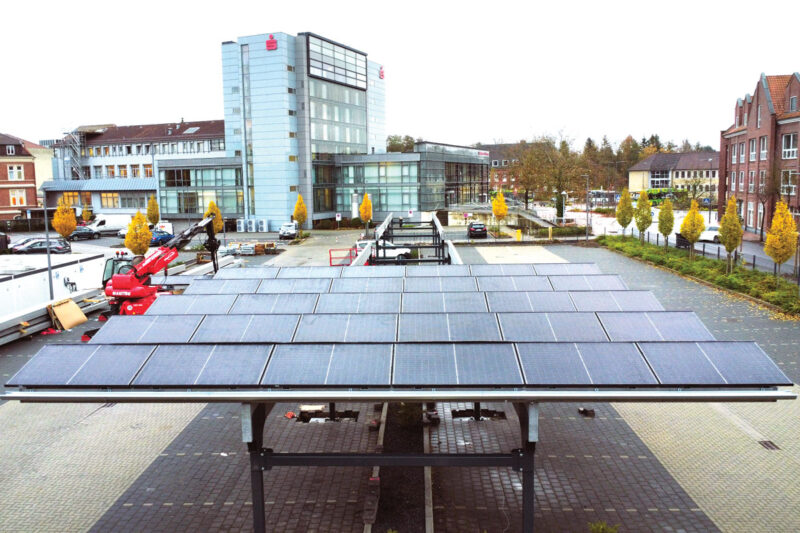 Solarcarport auf einem Parkplatz. Im Hintergrund das Gebäude der Sparkasse.