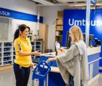 In einem IKEA-Geschäft reicht eine Kunden einer IKEA-Mitarbeiterin einen Kassenzettel, um ein Produkt abzuholen.