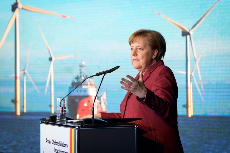 Bundeskanzlerin Merkel bei einer Rede im Hintergrund Fotos von Windkraftanlagen.
