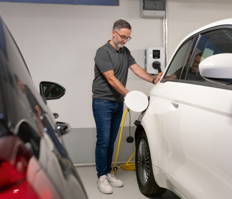 Mann lädt Auto mit Strom in einer Tiefgarage.