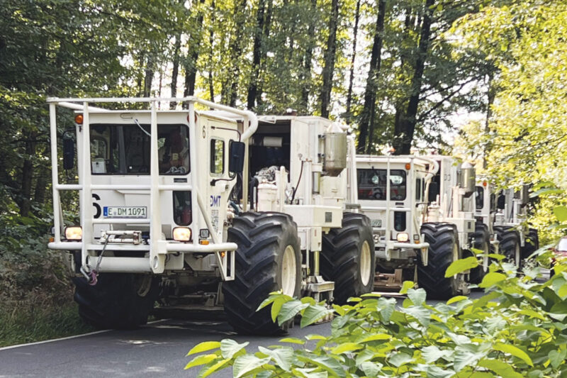 Eine Kolonne von Seismotrucks auf einem asphaltierten Waldweg