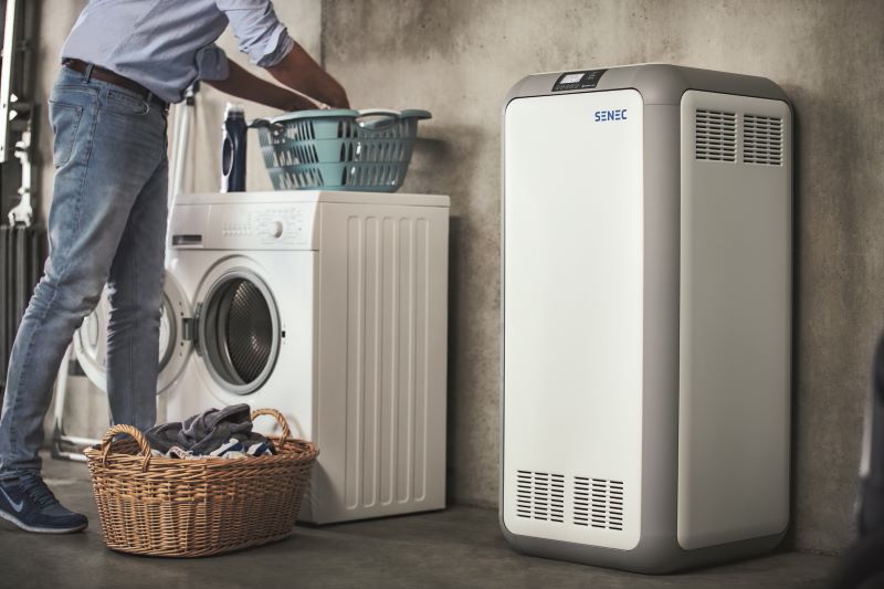 Ein Stromspeicher der Firma Senec steht in einer Waschküche, in der ein Mann die Waschmaschine bedient.